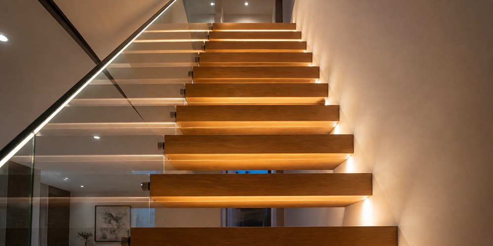 Wall-side floating wood treads with under-tread lighting and a glass balustrade.